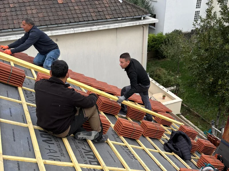 Trois couvreurs posant liteaux et tuiles en terre cuite sur un écran sous-toiture